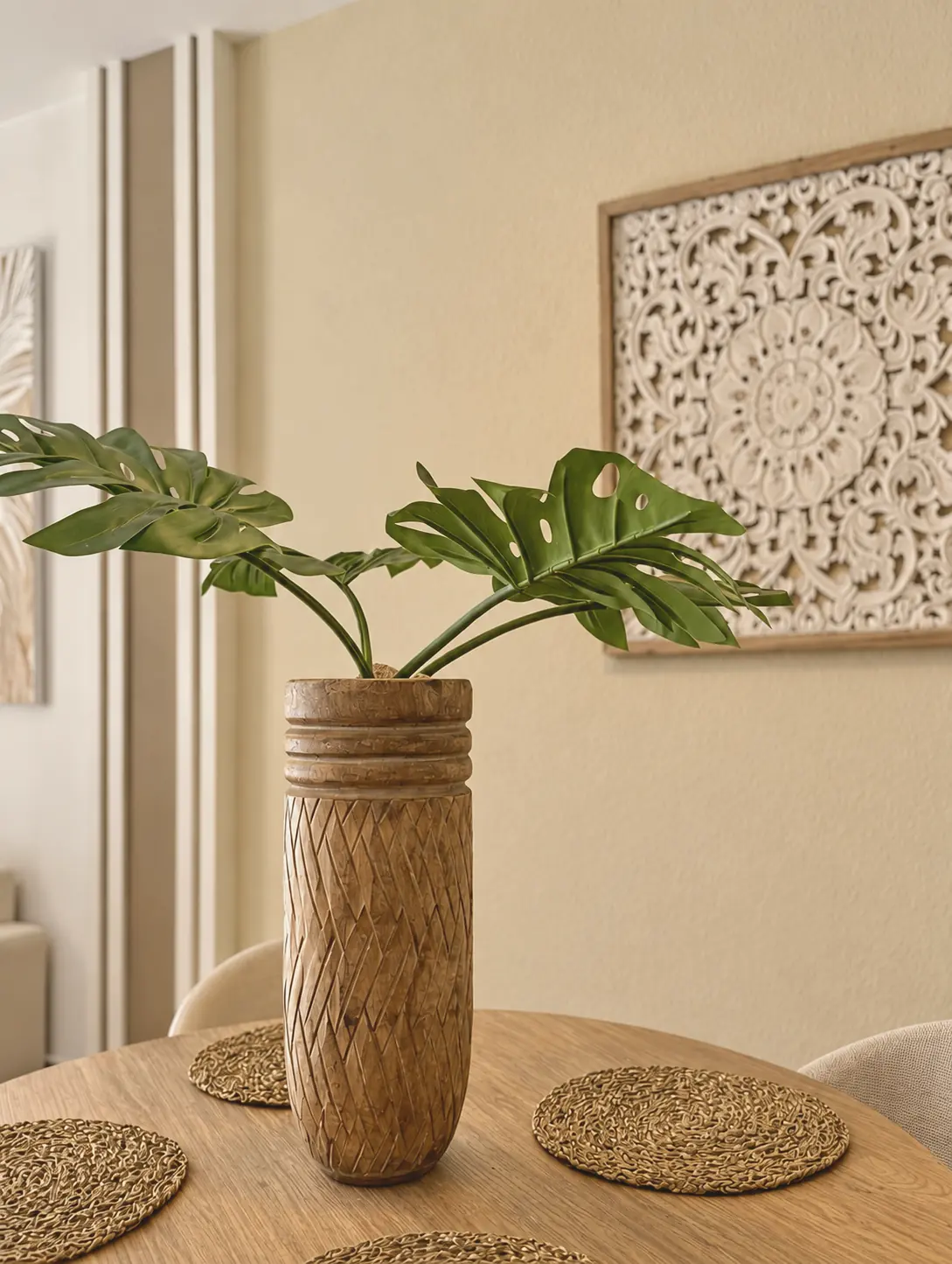 Comedor con jarrón de madera tallada, monstera y panel calado en la pared