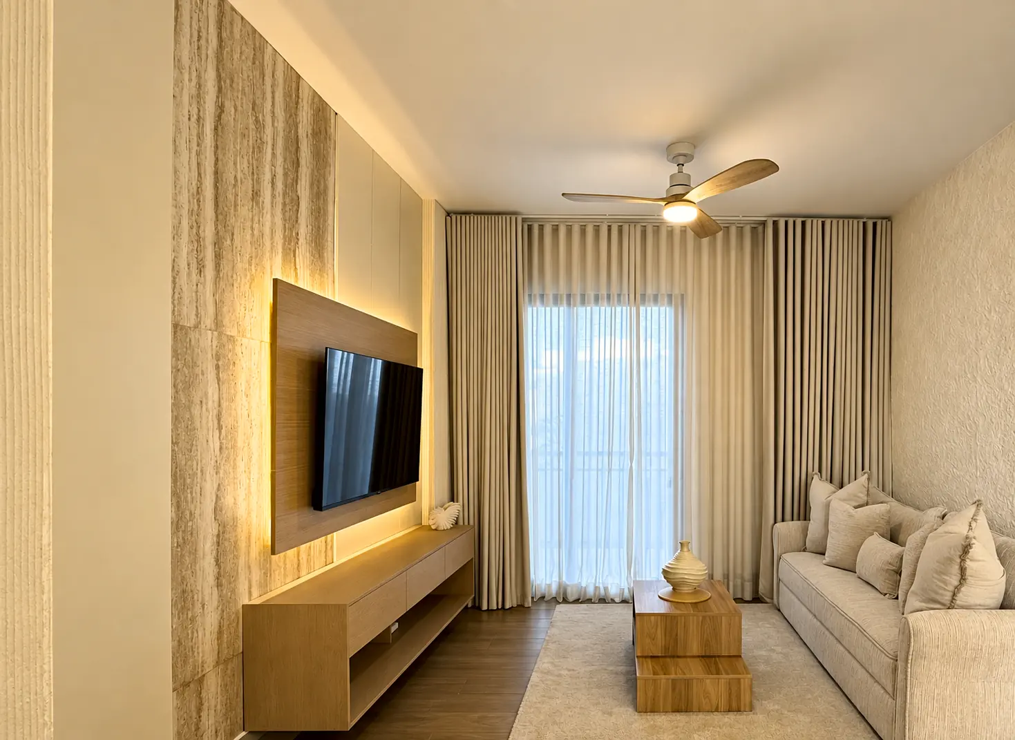 Sala de la residencia privada: pared de travertino, mueble de roble con luz cálida y cortinas de lino